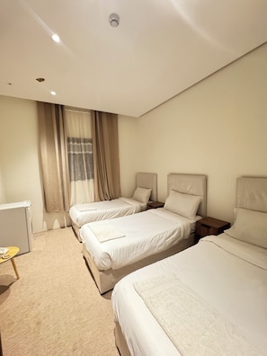 A hotel room with two beds, a small table, and a window with curtains. - Shaza Asil Hotel (Makkah)