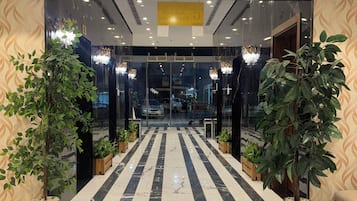 A hotel entrance with a marble floor, potted plants, and a chandelier.