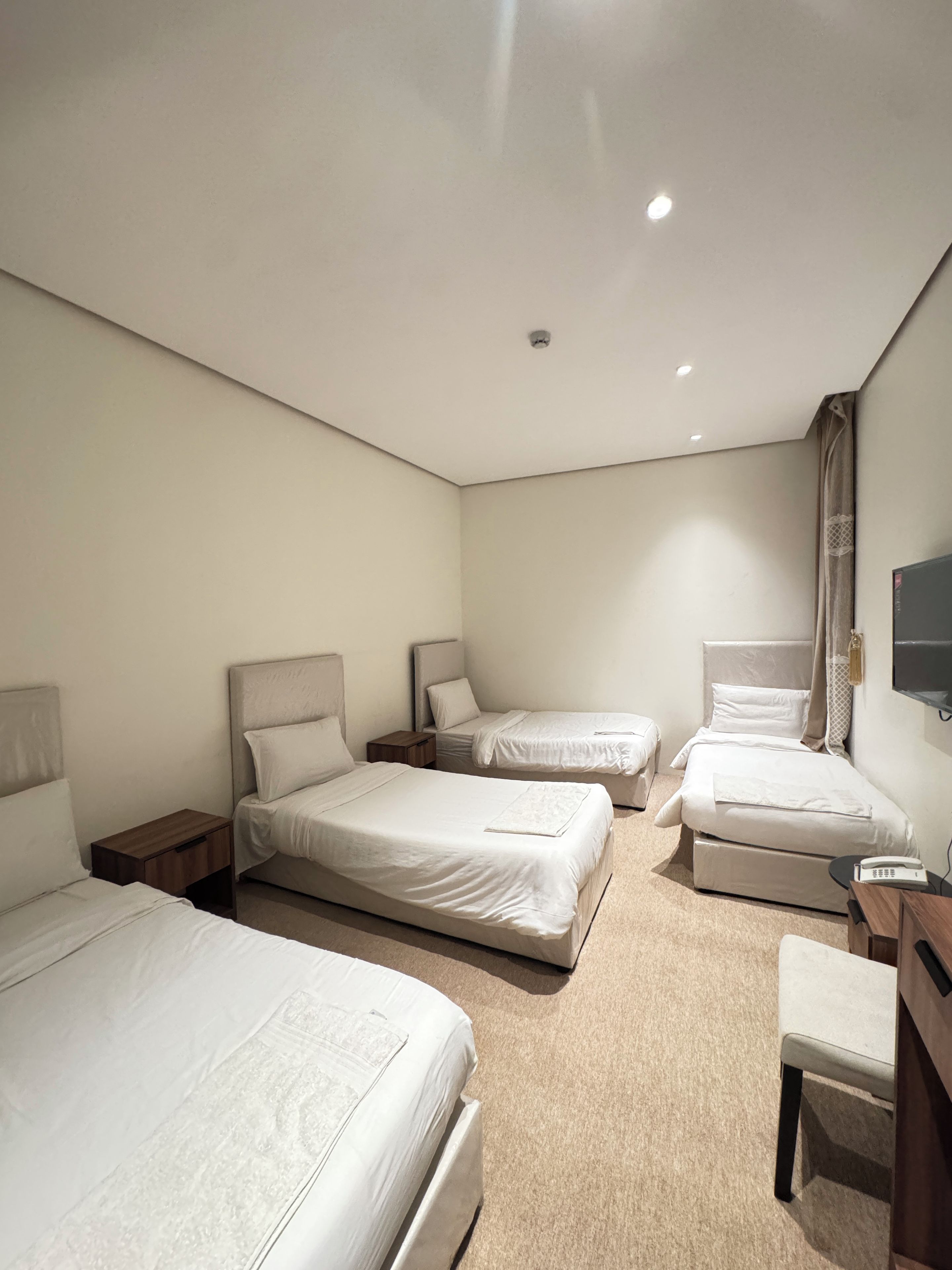 Hotellihuone, jossa on kolme sänkyä, työpöytä, tuoli ja televisio.