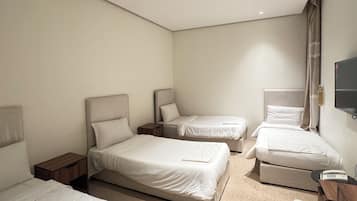A hotel room with three beds, a desk, a chair, and a television.