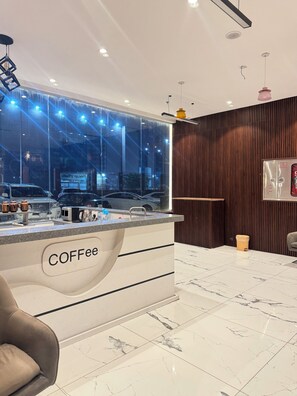 Estação de café moderna com bancada de mármore e pia, painéis de parede de madeira e vista para carros estacionados lá fora.