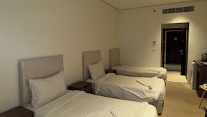 Ett hotellrum med tre sängar placerade i en rad, ett litet bord och en dörr som leder ut till en korridor.