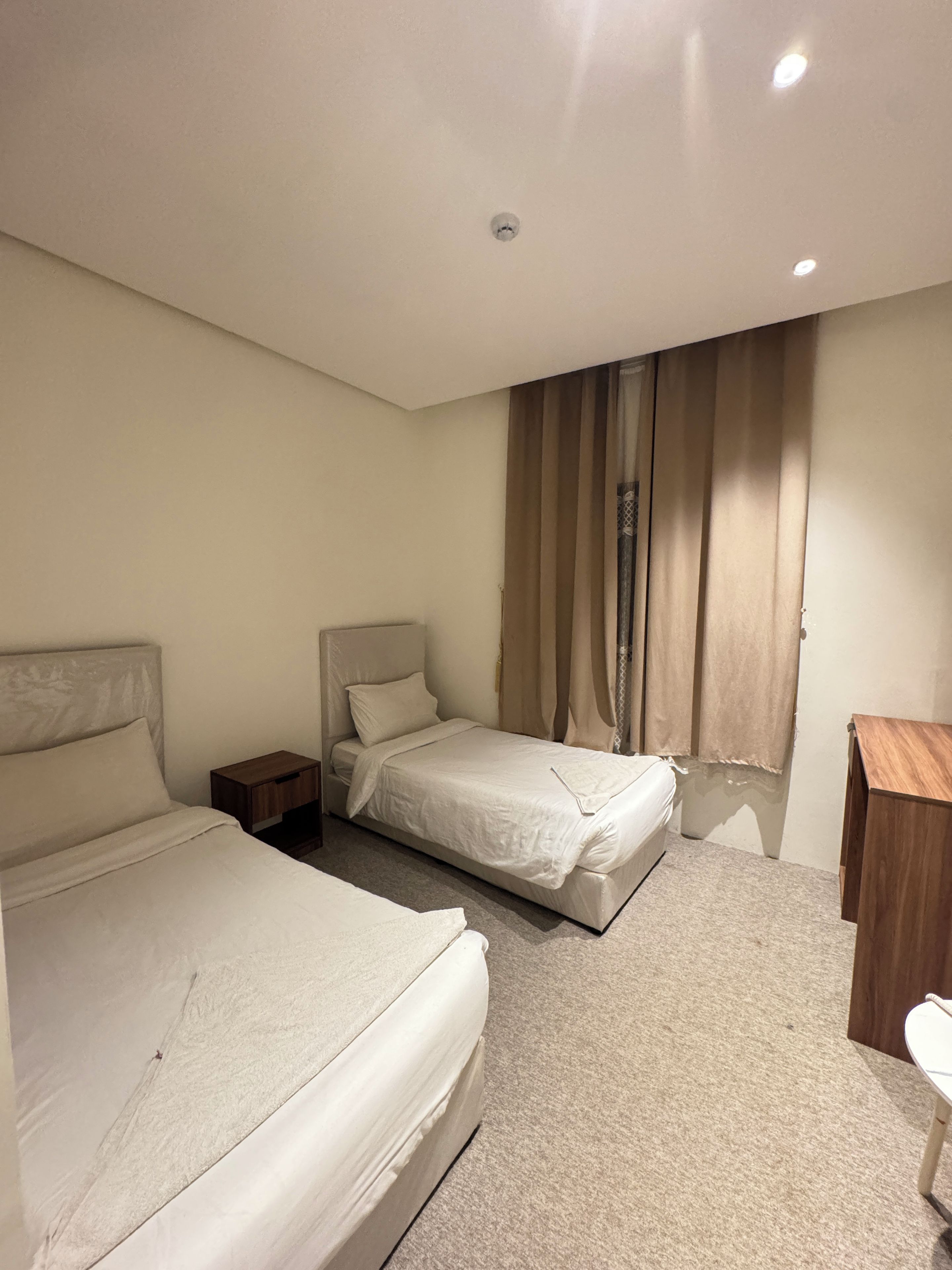 Ein Hotelzimmer mit zwei Betten, einem Holznachttisch, einem Schreibtisch und einem Fenster mit Vorhängen.