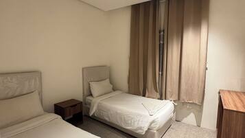 Ein Hotelzimmer mit zwei Betten, einem Holznachttisch, einem Schreibtisch und einem Fenster mit Vorhängen.