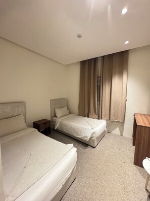 A hotel room with two beds, a wooden nightstand, a desk, and a window with curtains. - Shaza Asil Hotel (Makkah)