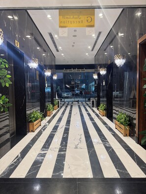 Um saguão de hotel com piso de mármore, plantas em vasos, lustres e um balcão de recepção.