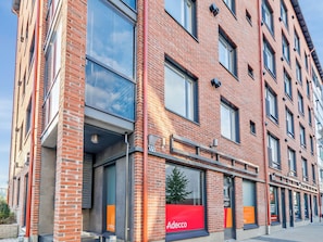 En flervåningsbyggnad i tegel med stora fönster och en butikslokal i bottenvåningen.