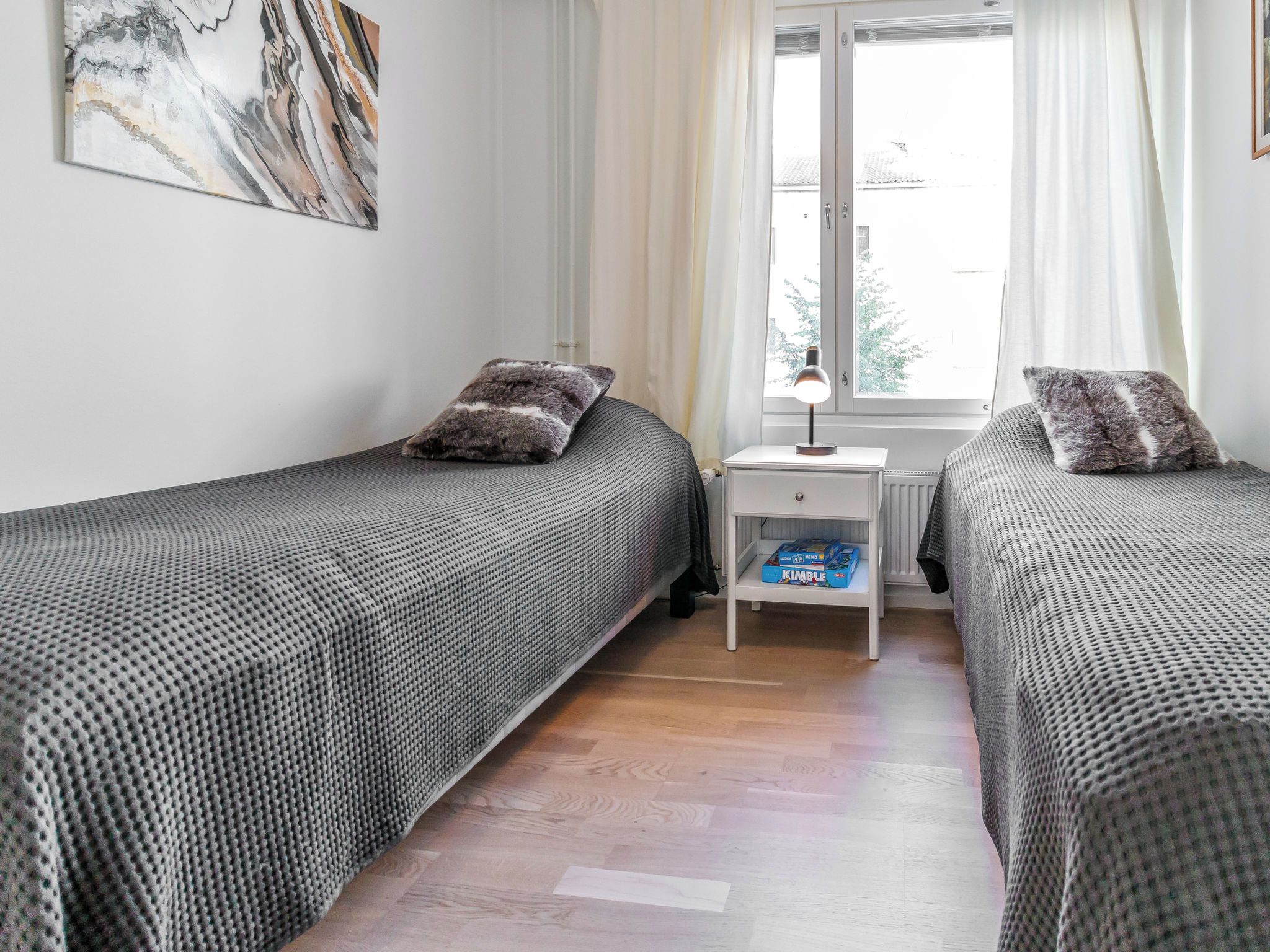 Un dormitorio con dos camas individuales, una mesita de noche con lámpara y una ventana con cortinas.