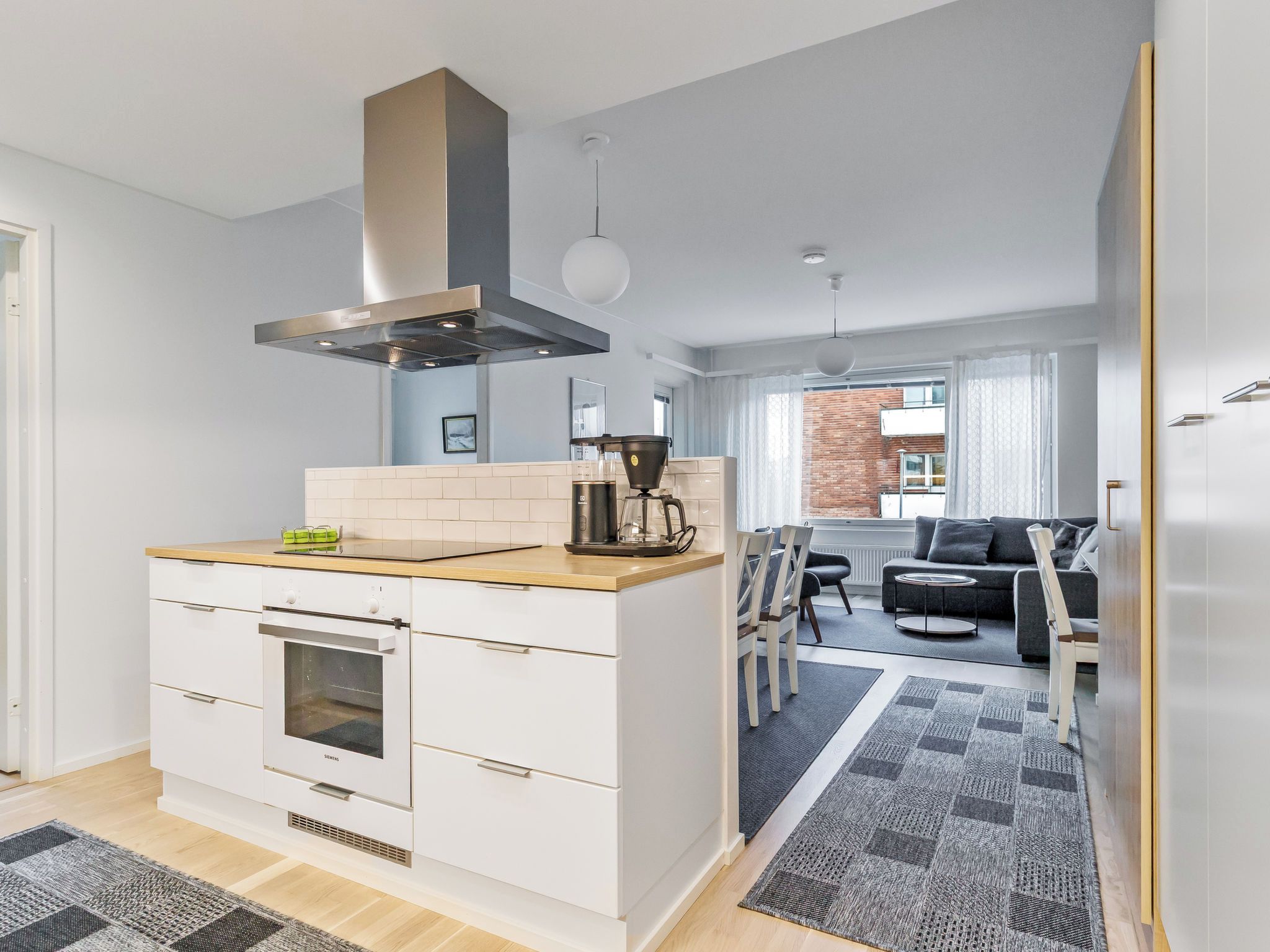 A modern kitchen with a built-in oven, a coffee maker, and a hanging light fixture.
