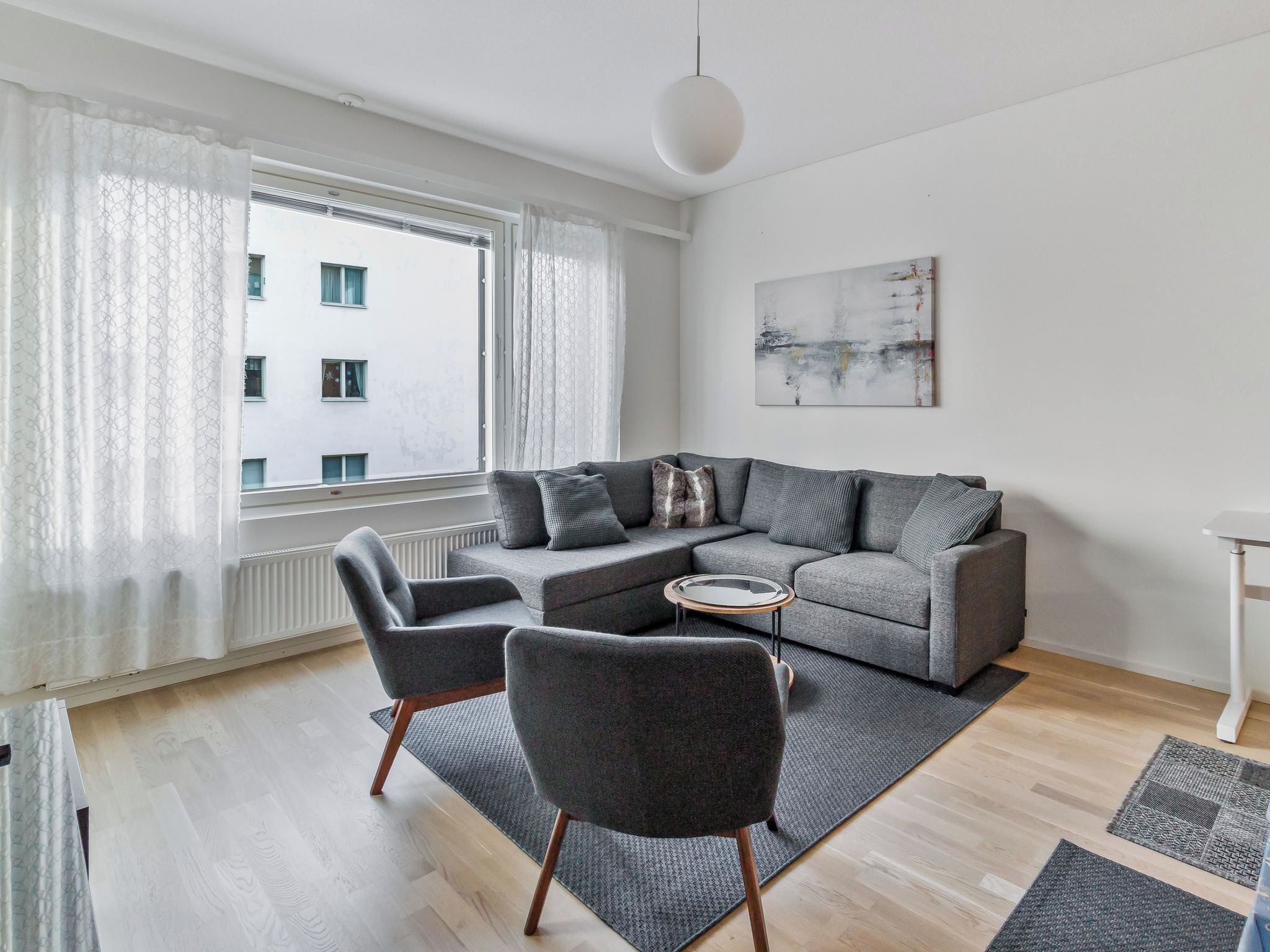 Una sala de estar moderna con un sofá gris, dos sillones, una mesa de centro y un amplio ventanal con cortinas.