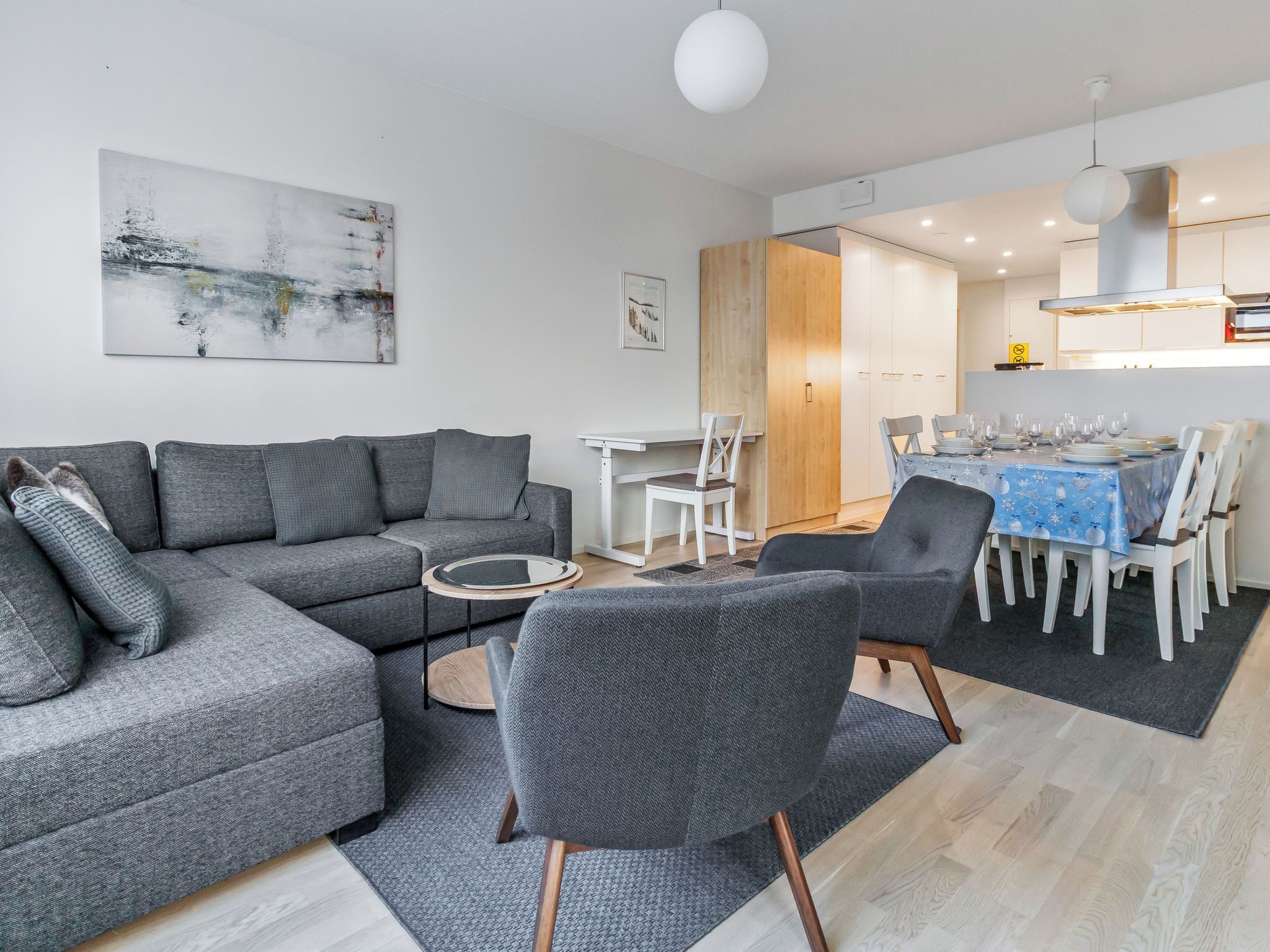 Una sala de estar moderna con un sofá seccional gris, una pequeña mesa de centro y un comedor con mantel azul.