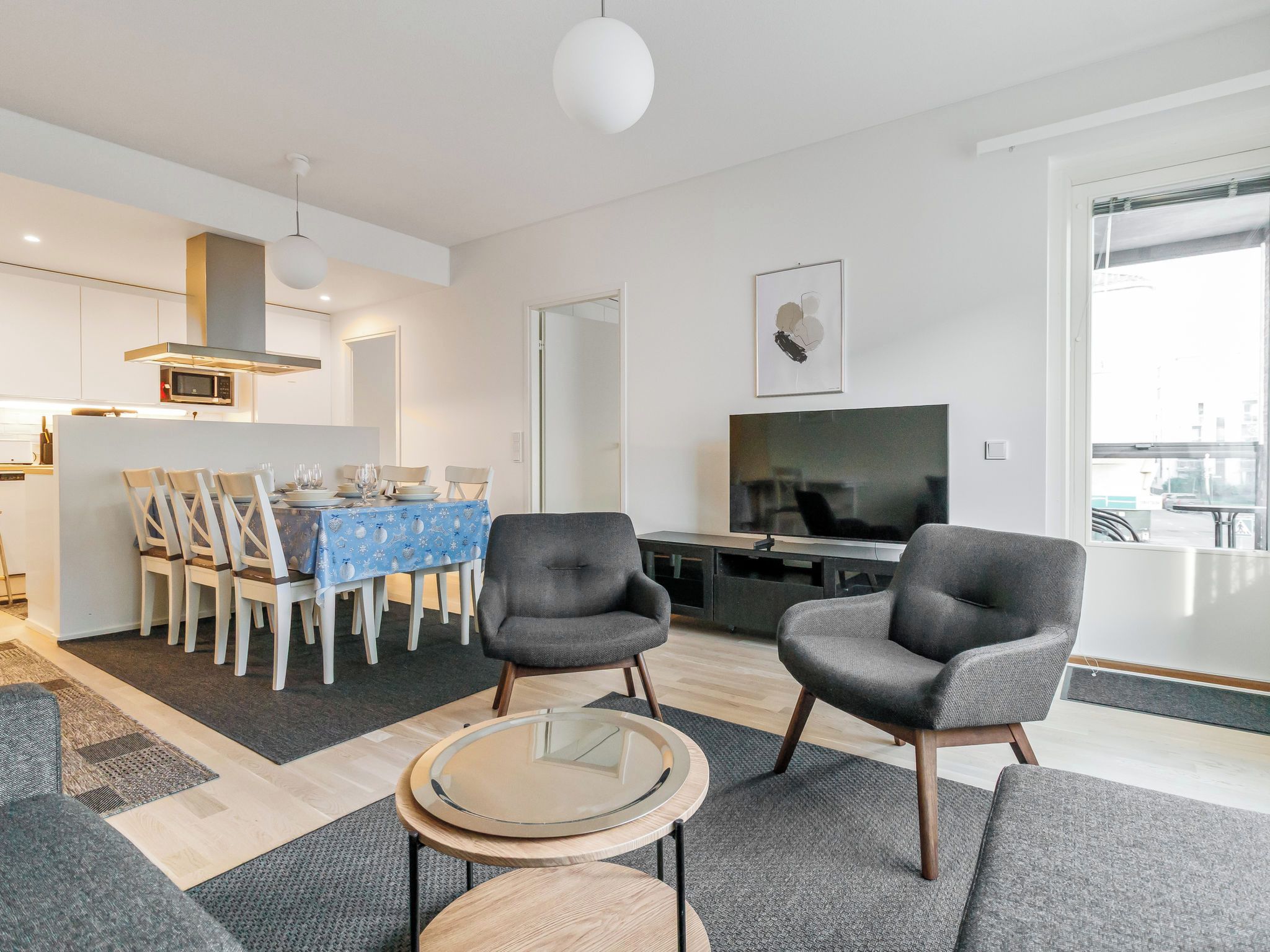 A modern living room with a dining area, a flat-screen TV, and a kitchen in the background.