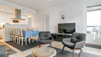 A modern living room with a dining area, a flat-screen TV, and a kitchen in the background.