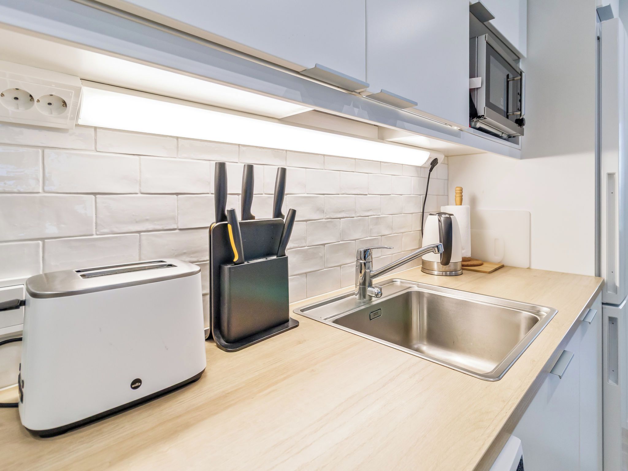 A modern kitchen with a built-in toaster, a knife block, a sink, and a microwave.