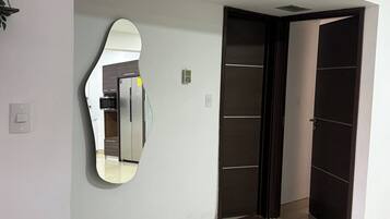 Un pasillo con un espejo grande, una puerta y una rejilla de ventilación en el techo.