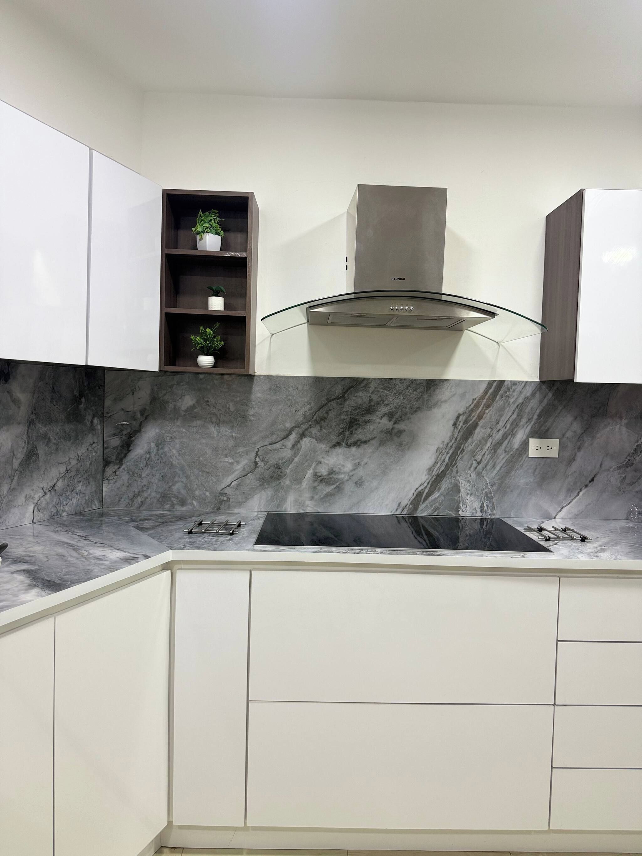 Een moderne keuken met witte kasten, een marmeren spatwand en een roestvrijstalen afzuigkap.