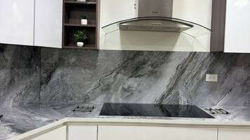 Een moderne keuken met witte kasten, een marmeren spatwand en een roestvrijstalen afzuigkap.