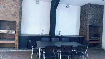 Un espacio de comedor al aire libre con pared de piedra, chimenea de ladrillo y una gran mesa con sillas.