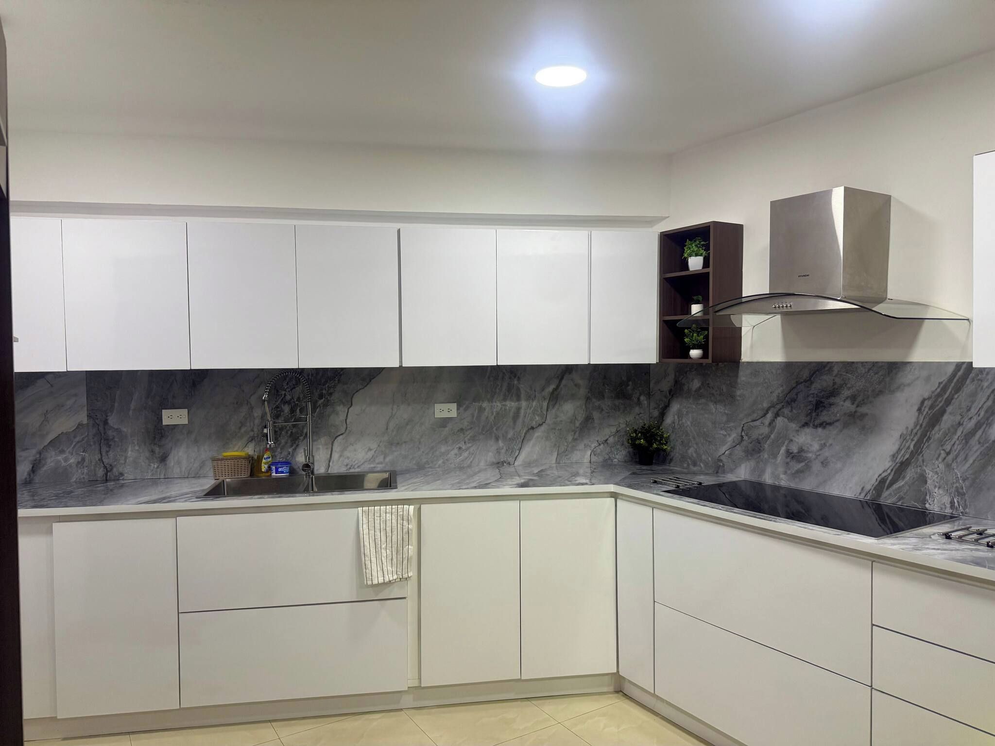 Eine moderne Küche mit weißen Schränken, einer Marmor-Spritzschutzleiste, einer Edelstahl-Spüle und einer eingebauten Dunstabzugshaube.