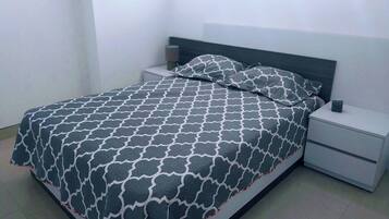 A neatly made bed with a patterned bedspread, a pillow, and a bedside table with a lamp.