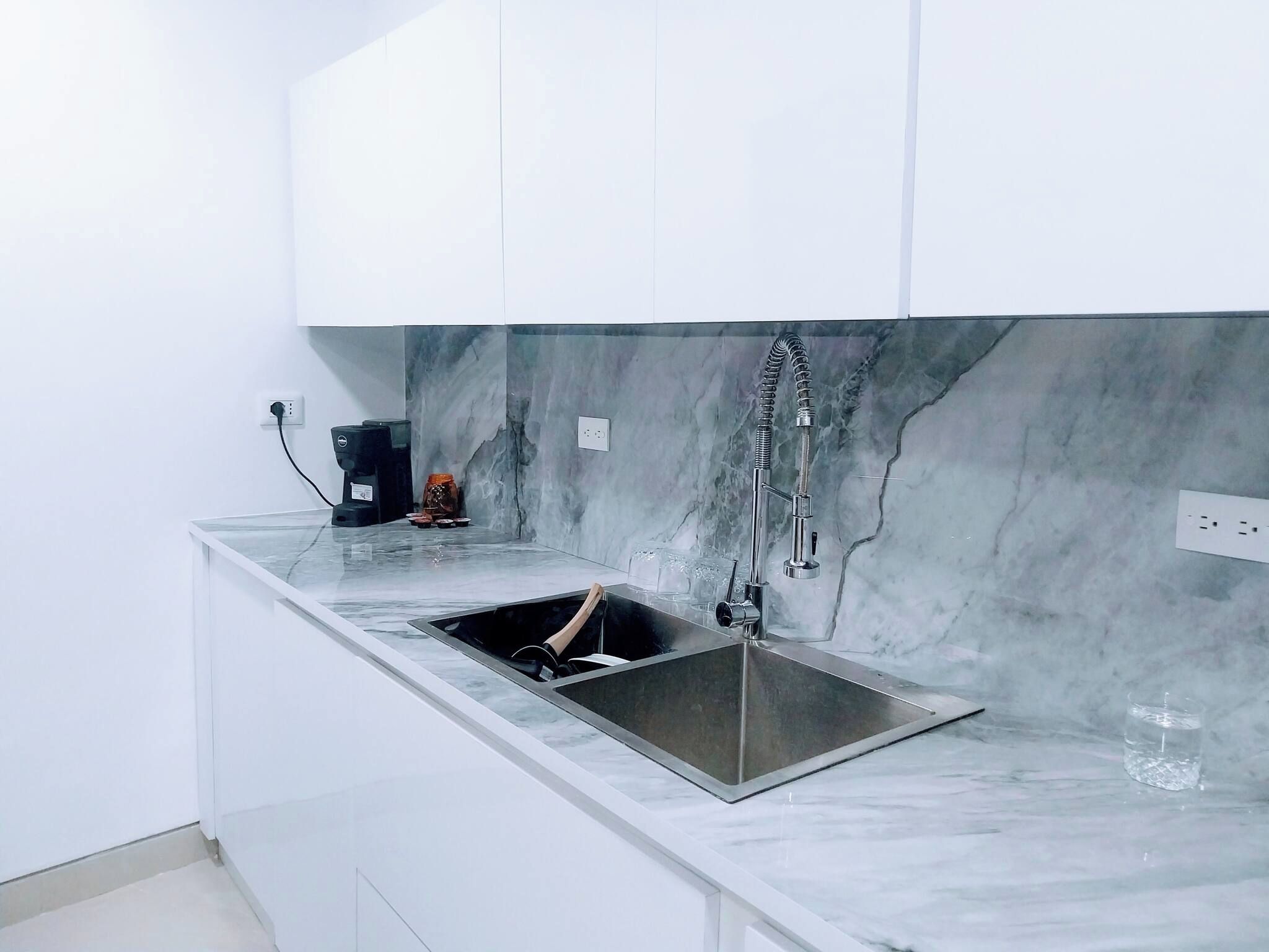 Una cocina moderna con un lavamanos de acero inoxidable, una cafetera y un salpicadero de mármol.
