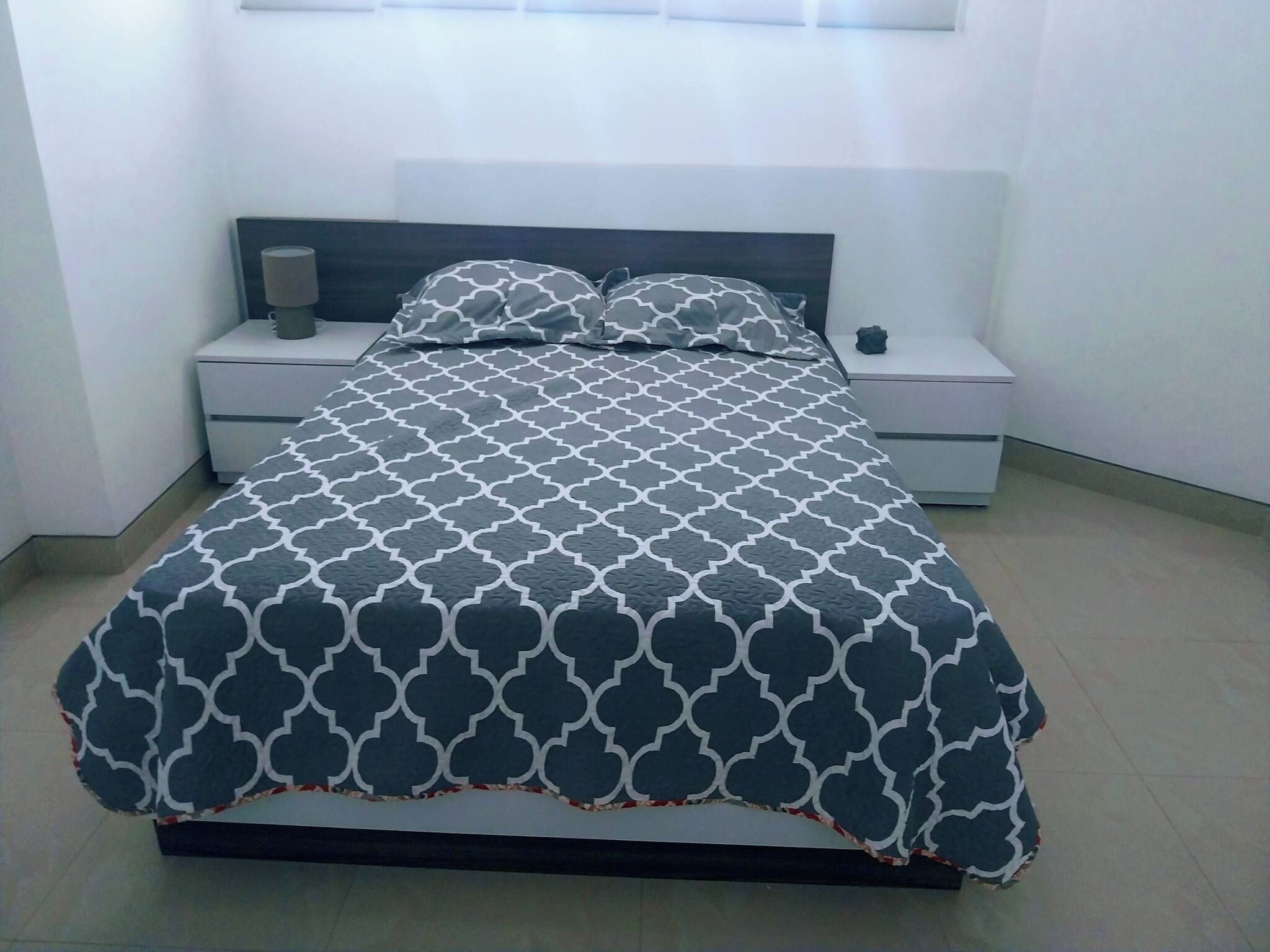 Een bed met een beddegoed met een patroon, twee nachtkastjes, een lamp en een nachtkastje.