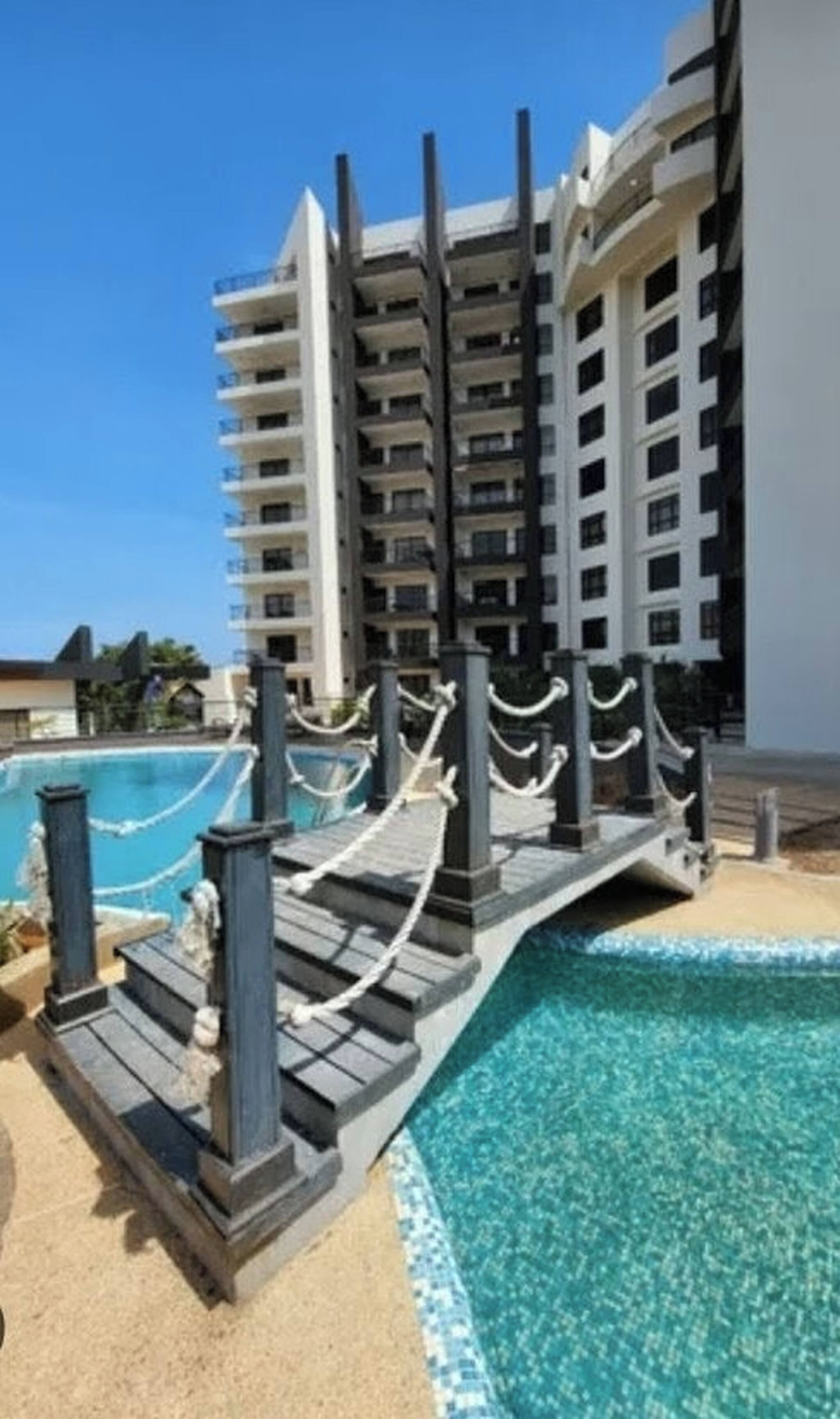 A swimming pool with a wooden deck and railings, surrounded by a high-rise building.