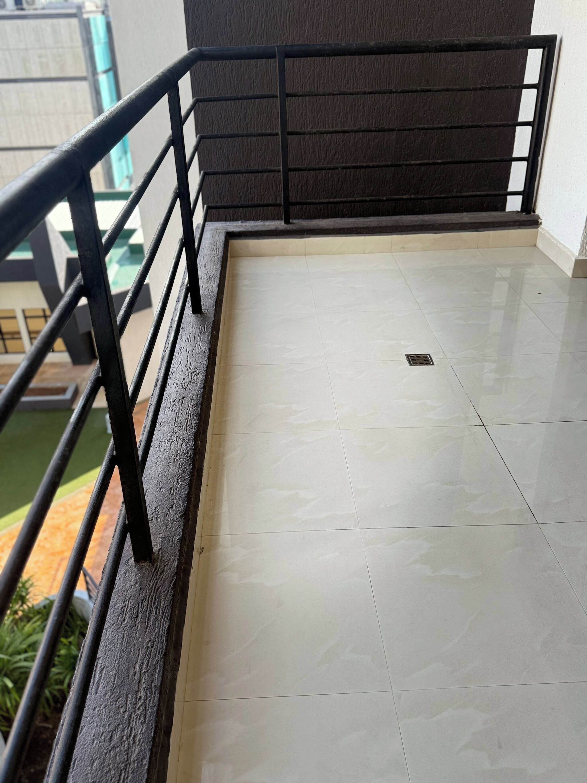 Un balcón con baranda metálica, piso de baldosas y vista a un edificio al fondo.