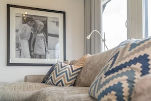 Ein Wohnzimmer mit einer Couch, gemusterten Kissen, einem gerahmten Foto an der Wand und einer Stehlampe.