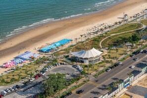 Vista aérea de una zona de playa con estacionamiento, sombrillas y un edificio con estructura en forma de cúpula.