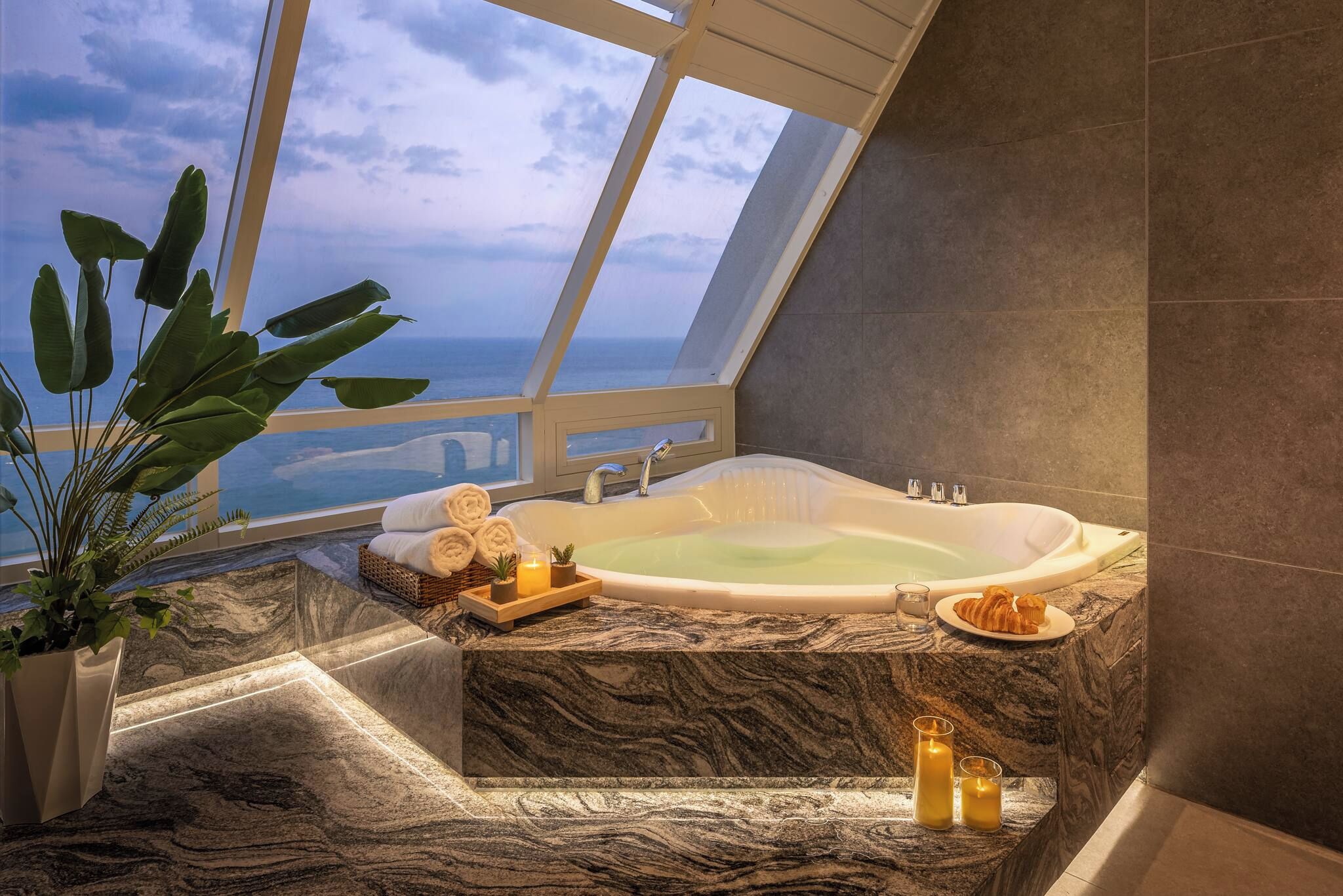 Une salle de bain aux hauts plafonds, dotée d’une grande baignoire, d’un sol en marbre et offrant une vue sur l’océan.