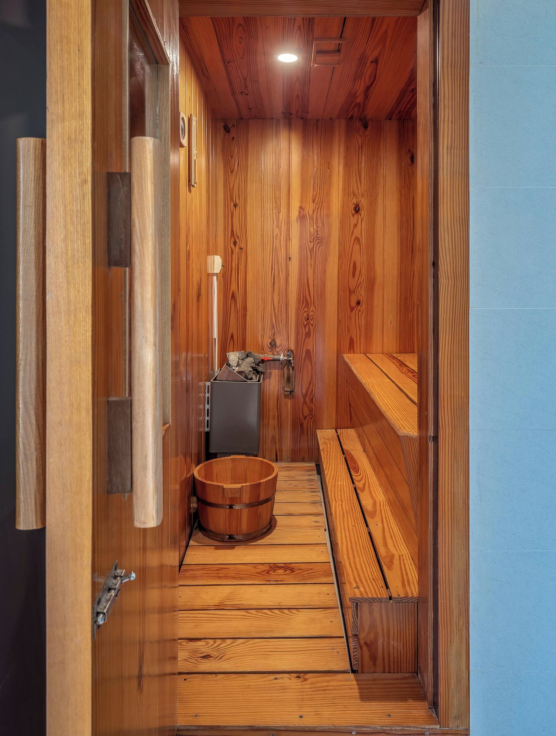 A sauna room with wooden walls, a bench, a wooden bucket, and a small heater.