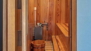 A sauna room with wooden walls, a bench, a wooden bucket, and a small heater.