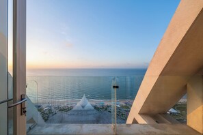 Une vue depuis un balcon donnant sur une plage, avec une structure blanche originale qui se distingue à l’horizon.