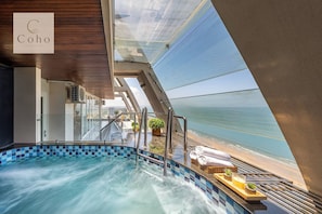 Una piscina con vista al mar, un área de descanso con barandilla de cristal y un letrero con la palabra 'Coho'.