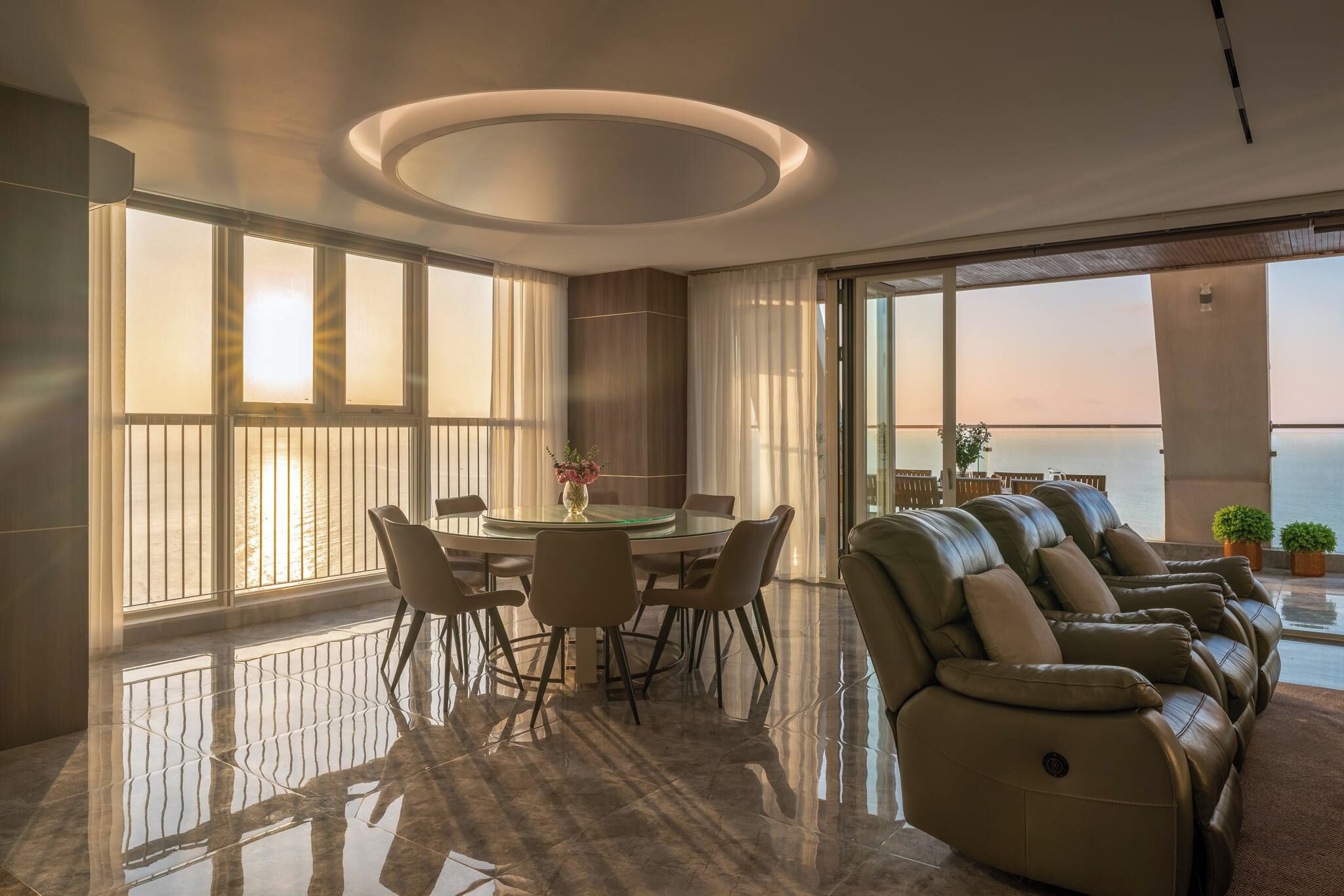 A modern interior with a dining area, a sofa, and large windows overlooking a body of water.
