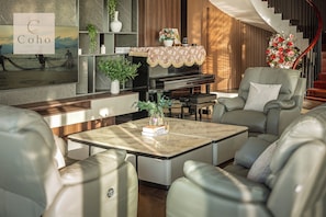 Un salon moderne avec des canapés en cuir, une table basse, un piano et un escalier agrémenté d’un arrangement floral.