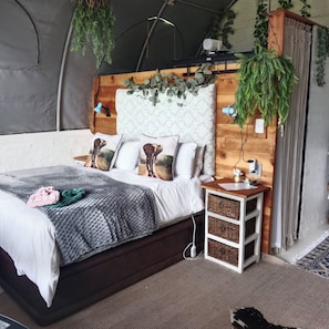 Telttakattoinen huone, jossa on sänky, yöpöydät ja roikkuvia kasveja.