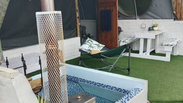 A pool area with a small hot tub, a hammock, and a covered seating area.