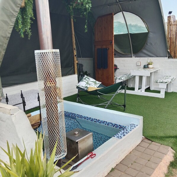 A pool area with a small hot tub, a hammock, and a covered seating area.