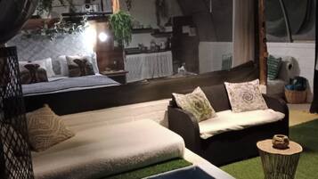 Eine Zelthotellunterkunft mit einer Couch, Kissen, einem kleinen Tisch und einem Poolbereich.