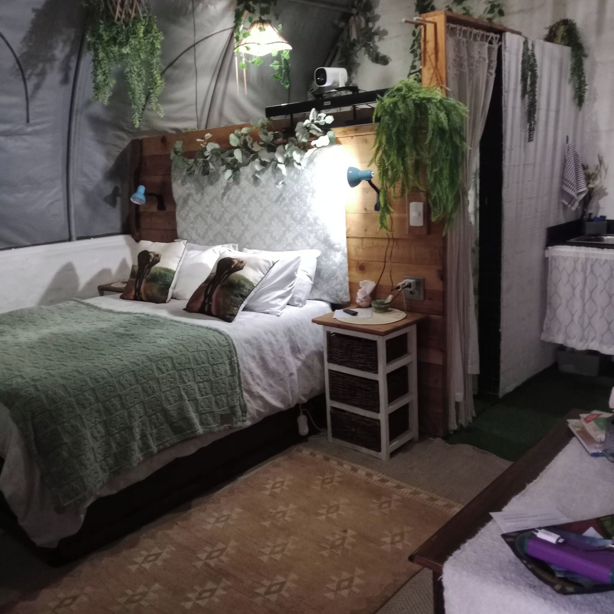 Une chambre à coucher avec un lit, une table de chevet, une lampe et des plantes suspendues.
