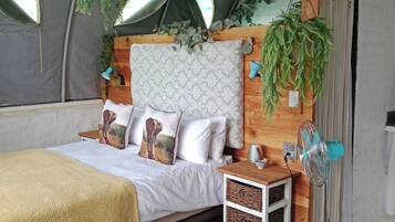 A tent-style bedroom with a bed, pillows, a fan, and hanging plants.