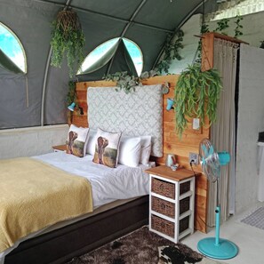 A tent-style bedroom with a bed, pillows, a fan, and hanging plants.