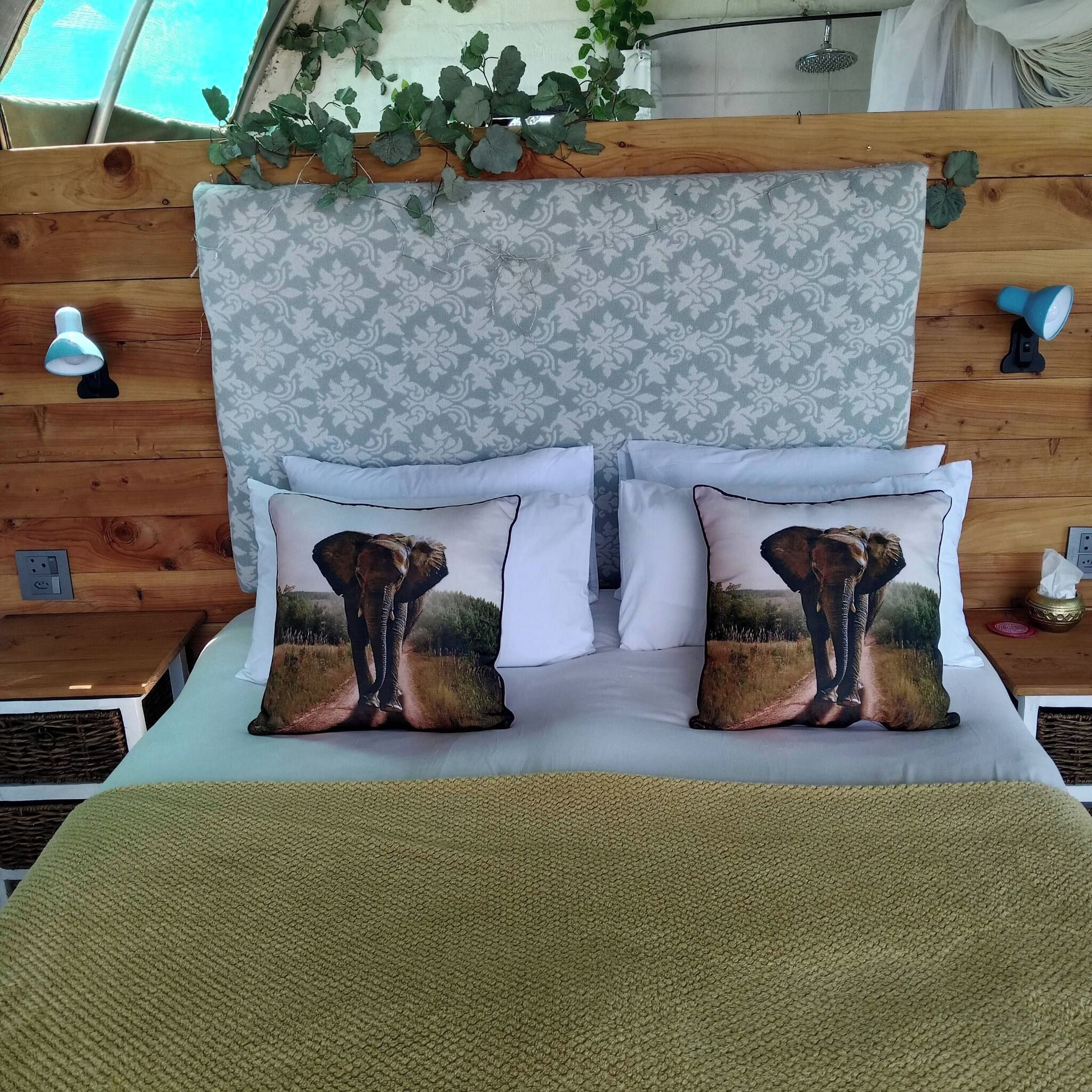 A bed with a patterned headboard, two pillows with an elephant print, and a green textured throw blanket.