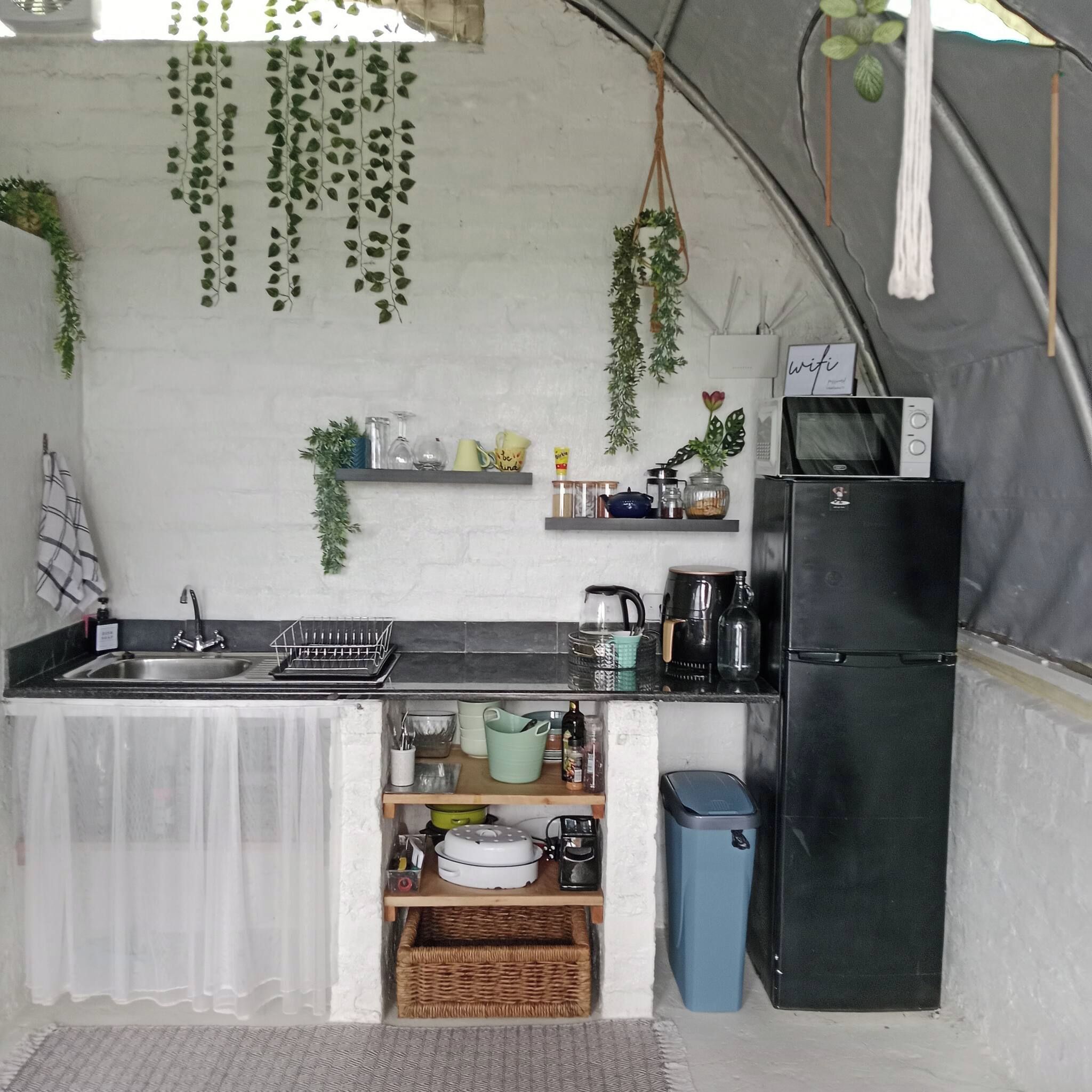 A compact kitchen with a sink, a refrigerator, and shelves with various items.
