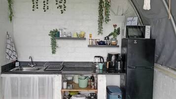 A compact kitchen with a sink, a refrigerator, and shelves with various items.