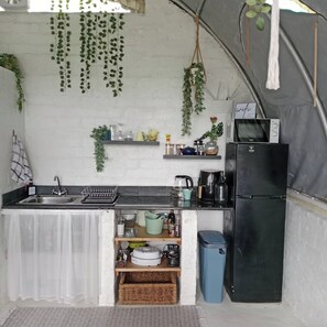 A compact kitchen with a sink, a refrigerator, and shelves with various items.