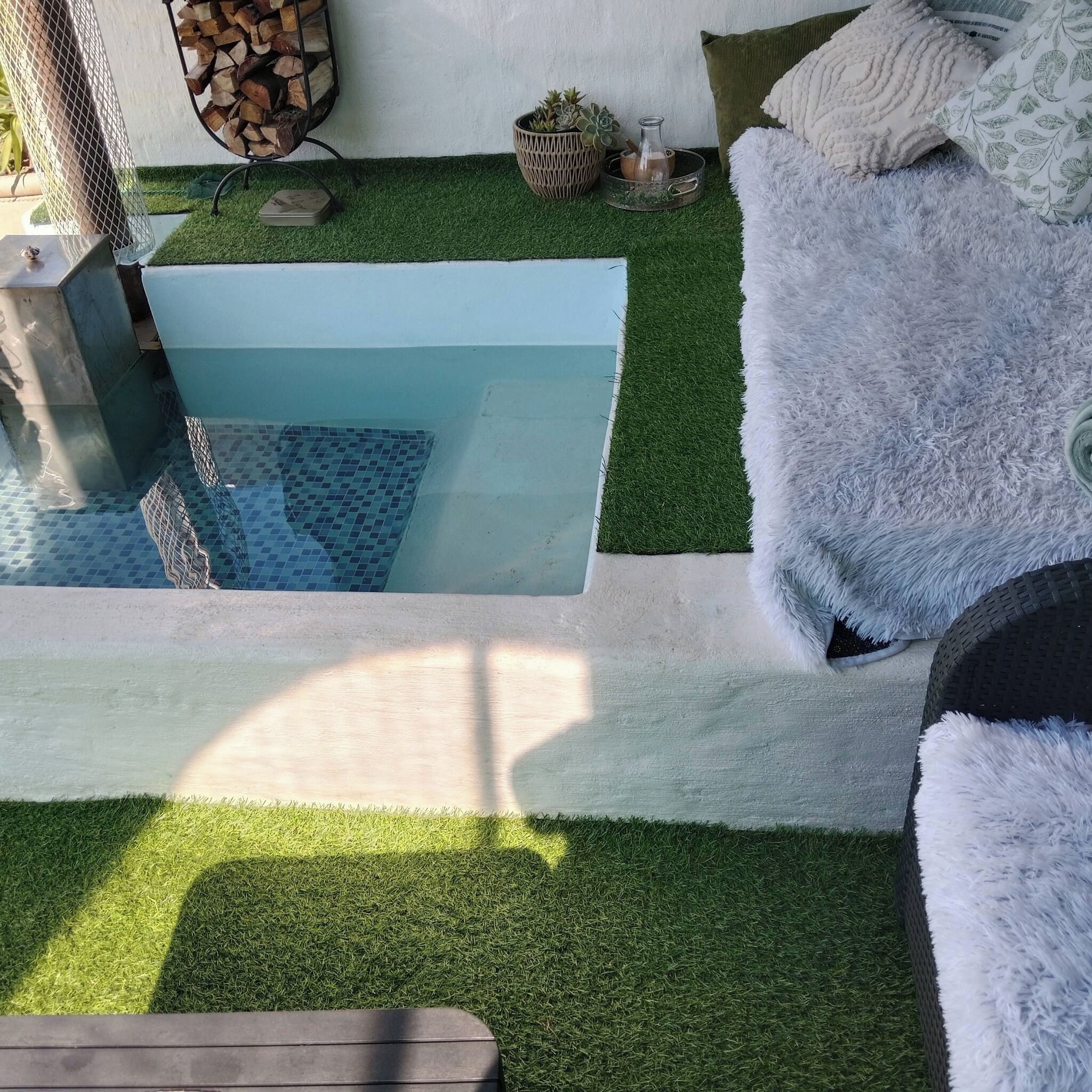Ein Pool mit Kunstrasen, ein weißes, flauschiges Sofa und ein Korbwannen mit einer Flasche.