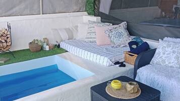 Un espace piscine avec une piscine aux couleurs blanche et bleue, un canapé avec des coussins et un fauteuil en osier.